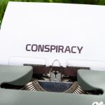 a close up of a typewriter with the word conspiracy on it
